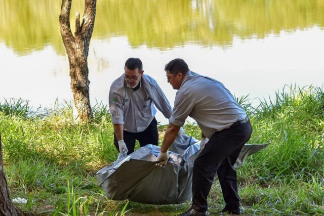 Uma foto dos agentes da funerária removendo o corpo das margens da lagoa