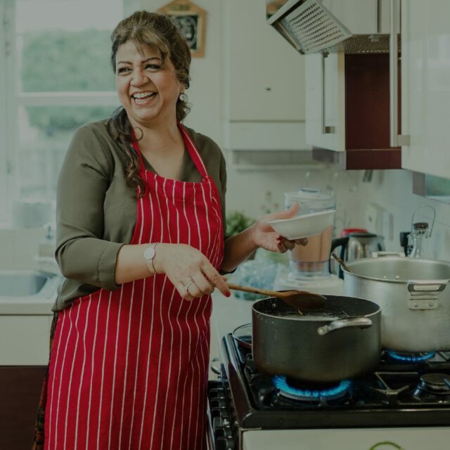 Uma foto de uma mulher cozinhando com o gás natural encanado da Comgás